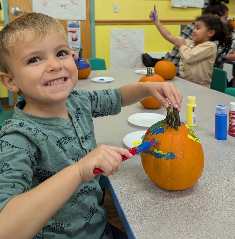 Child smiling while painting a pumpkin.