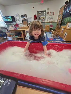 Child smiling with her hands in soapy water.